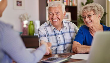 Older couple discussing retirement plans with an advisor, smiling and shaking hands at a table with financial documents and a calculator, reflecting the importance of 401(k) and retirement planning for future financial security.