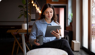 Young woman in a cozy café, holding a cup and using a tablet, representing personalized health insurance consultations.