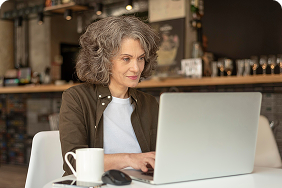 Senior woman using laptop in a café, engaged in online research for affordable final expense insurance options.