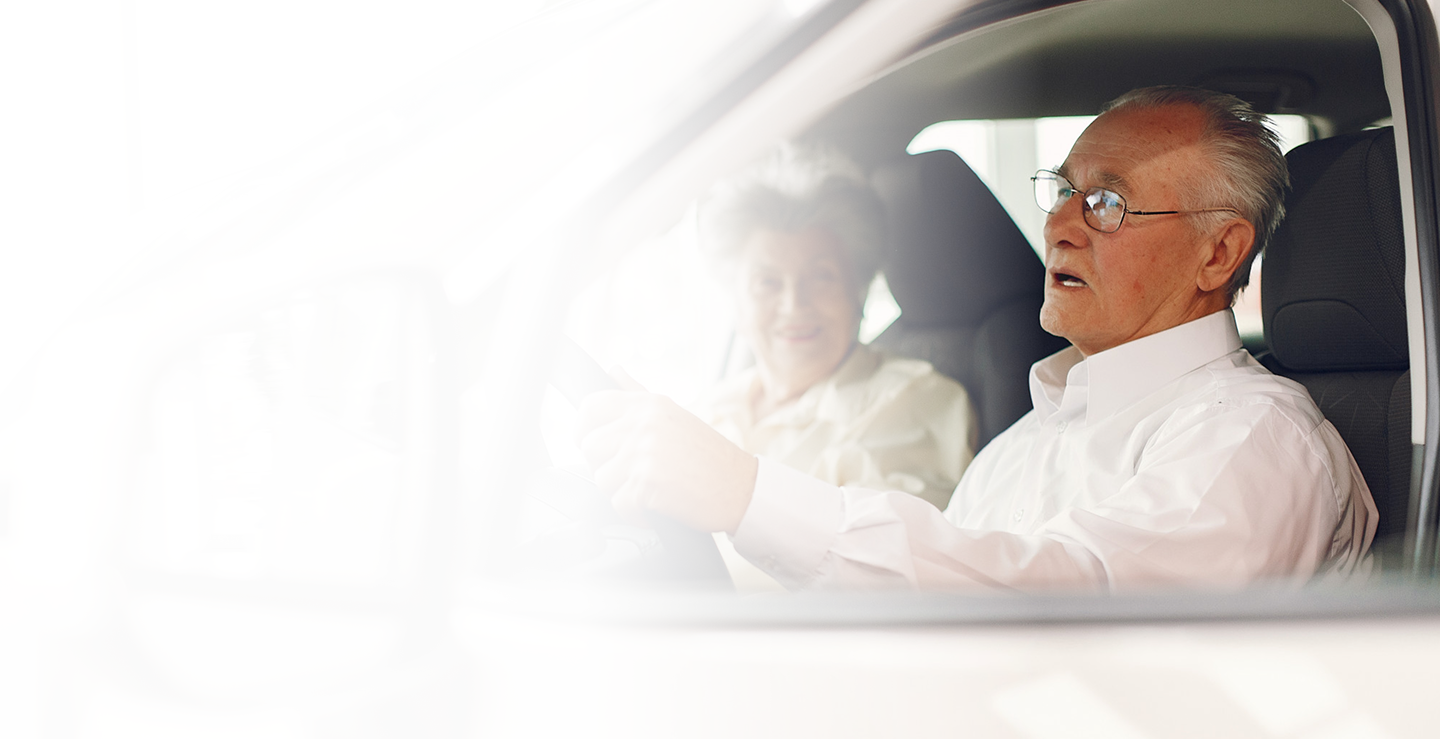Senior couple in a car, with the man driving and the woman smiling, representing safe and reliable auto insurance for seniors.