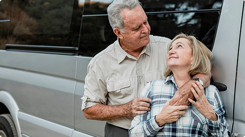 Senior couple smiling and interacting near a vehicle, representing the importance of auto insurance for mature drivers and emphasizing safety and companionship.