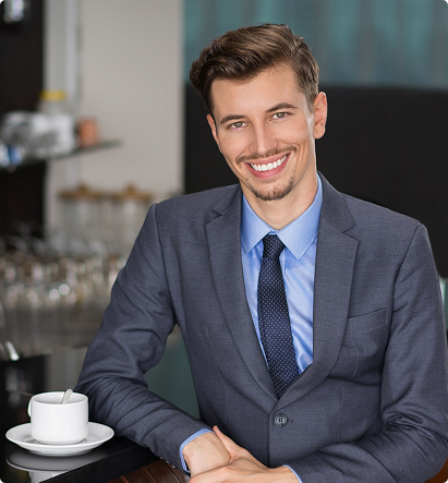 Smiling young man in a suit at a café, representing professionalism and client dedication in the insurance industry.