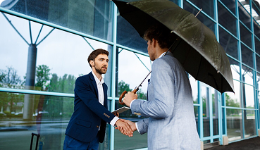 Business professionals shaking hands under an umbrella, symbolizing partnership and protection in commercial insurance.