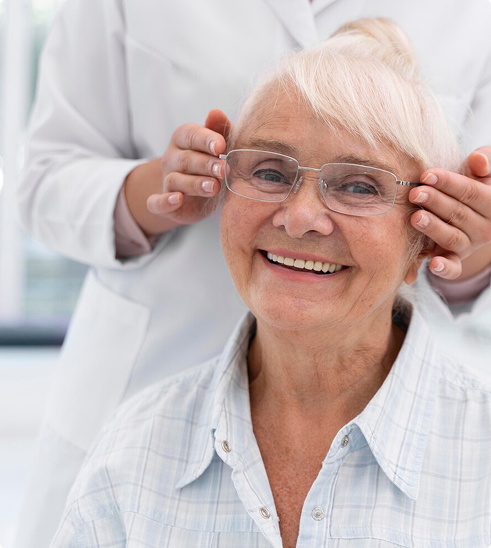 Senior woman smiling while adjusting her glasses during an eye exam, emphasizing the importance of vision care for seniors.