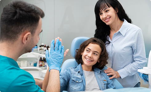 Child smiling in dental chair with dentist and mother, illustrating dental care and family-friendly insurance coverage options.