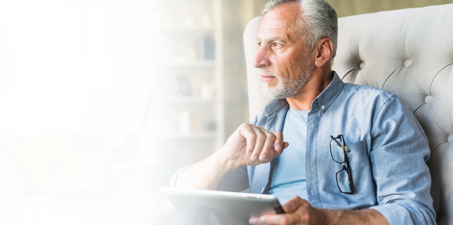 Senior man thoughtfully using a tablet while seated in a comfortable chair, emphasizing the importance of final expense insurance for peace of mind and financial security.