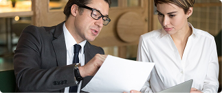 Professional discussion between a man in a suit and a woman in a white shirt, reviewing documents related to Indexed Universal Life insurance and financial planning.