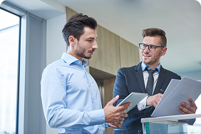 Two professionals discussing Indexed Universal Life insurance strategies, one holding a tablet and the other reviewing documents, in a modern office setting.
