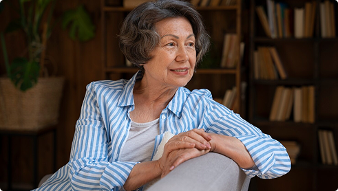 Senior woman in a striped shirt, seated comfortably, reflecting on Medicare options for retirement planning.