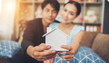 Couple holding a small model house, symbolizing mortgage protection and home security in the context of life insurance solutions.