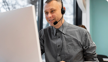 Man wearing a headset and gray shirt, providing ongoing client support while working on a computer, reflecting personalized assistance in private health insurance services.
