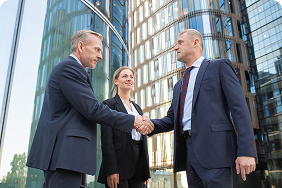 Business professionals shaking hands outside modern office buildings, symbolizing partnership and collaboration in group insurance solutions.