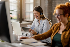 Two professionals collaborating in an office setting, one wearing a headset and using a tablet, while the other types on a laptop, highlighting teamwork and support in disability insurance services.