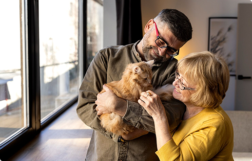 Couple joyfully holding a cat indoors, emphasizing the bond between pets and their owners, reflecting the importance of pet insurance for unexpected vet bills.