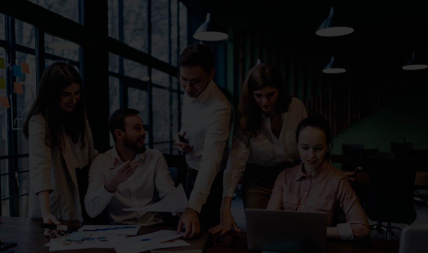 Group of professionals collaborating in a modern office setting, discussing documents and analyzing data on a laptop, emphasizing teamwork and business strategy for commercial insurance solutions.