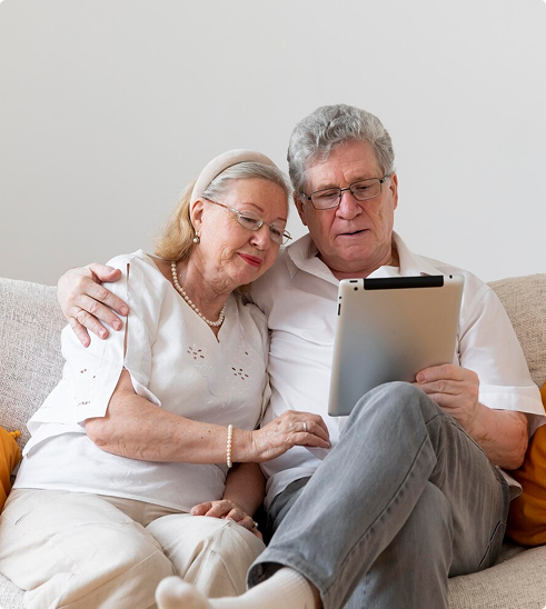 Senior couple sitting together on a couch, looking at a tablet, representing family connection and the importance of final expense insurance for seniors.