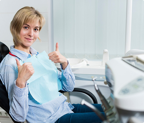 Smiling woman in a dental chair giving thumbs up, wearing a dental bib, representing positive dental care experience related to dental insurance coverage options.