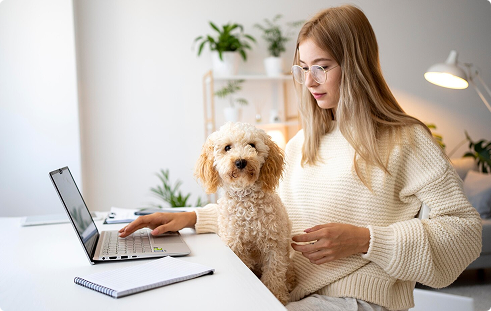 Woman working on a laptop at home with a small dog beside her, illustrating the companionship and support pets provide to their owners, relevant to pet insurance benefits.
