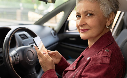 Senior woman in car using smartphone, representing personalized auto insurance solutions for seniors.