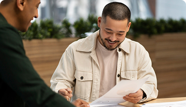 Smiling man reviewing documents with a colleague, illustrating collaboration in business insurance and employee benefits discussions.