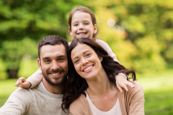 Smiling family of three, including a mother, father, and young daughter, enjoying a sunny day outdoors, representing the importance of family health and insurance coverage options.