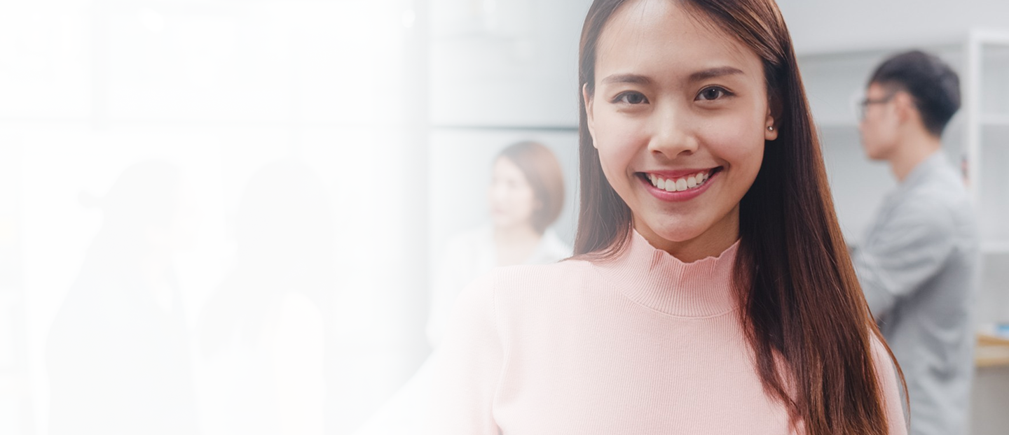 Smiling woman in a pink sweater with co-workers in a modern office setting, representing teamwork and employee support in business insurance.