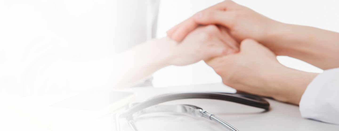 Hands of a healthcare professional and a patient engaged in a supportive gesture, with a stethoscope and smartphone visible on the table, symbolizing personalized health insurance solutions.