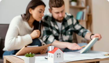 Couple reviewing home insurance options with a miniature house model and paperwork on a table, emphasizing homeowners insurance and asset protection.