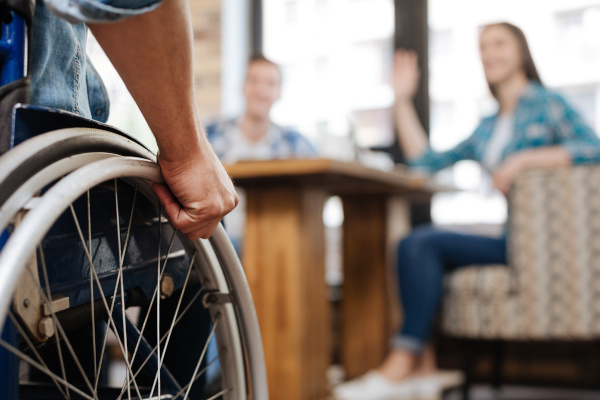 Person holding a wheelchair, engaging with two individuals in a casual meeting setting, emphasizing disability support and personal insurance discussions.